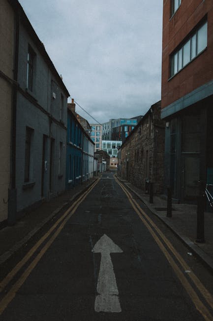 A narrow street scene in Chiswick, featuring cobblestone pavement with tactile paving strips along the edges. Flanked by tall, closely spaced historic buildings with detailed facades, some with fire e